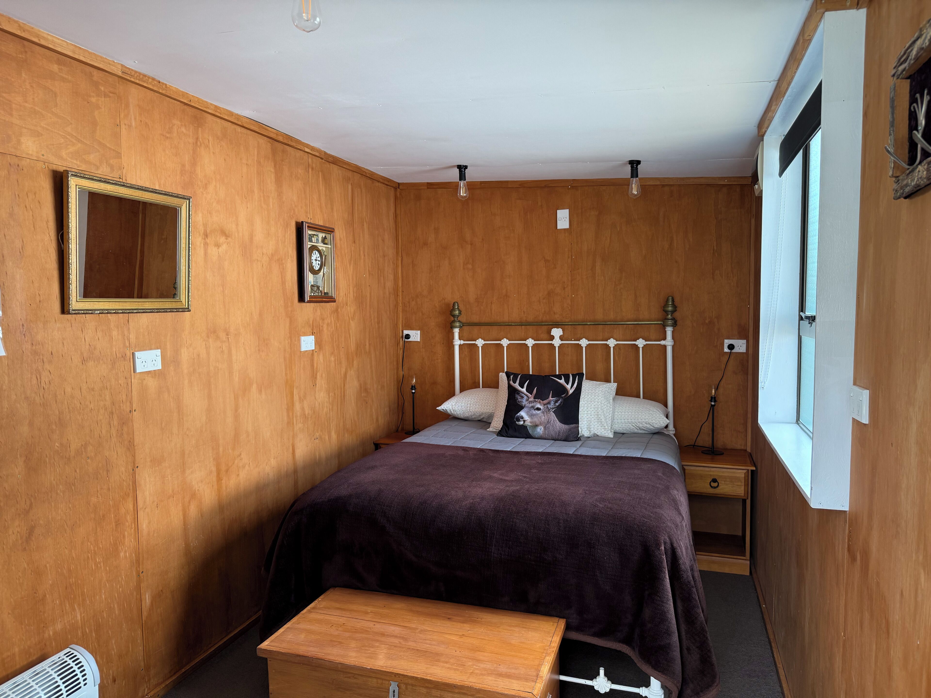 Una habitación con paneles de madera, una cama, una mesita de noche y una ventana.
