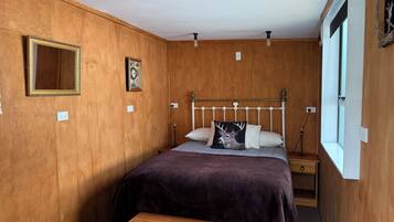 Una habitación con paneles de madera, una cama, una mesita de noche y una ventana.