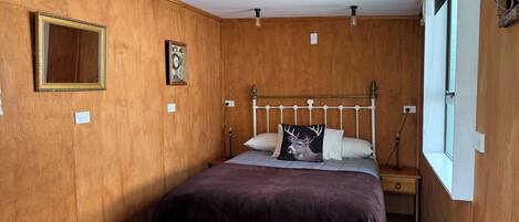Una habitación con paneles de madera, una cama, una mesita de noche y una ventana.