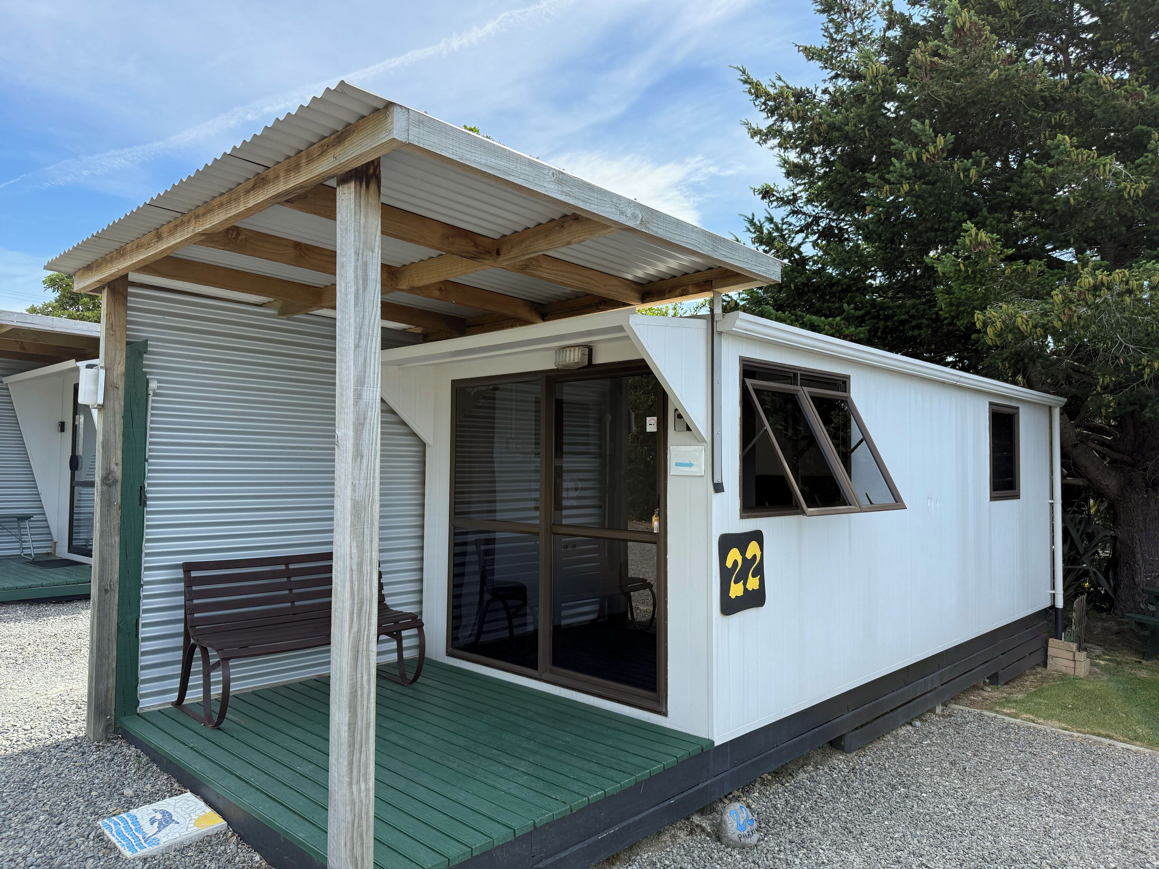A small, single-story mobile home with a covered porch, a bench, and a door with a window.