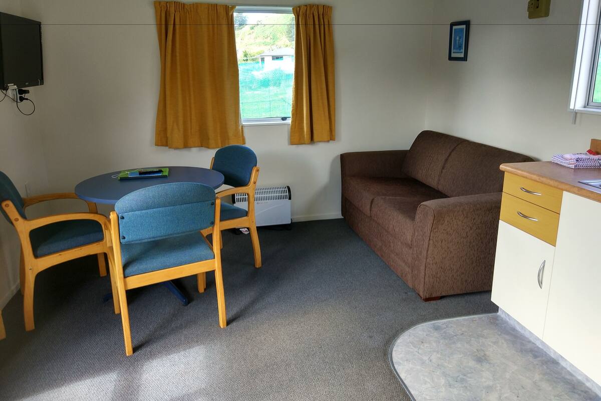 A compact room with a dining table, two chairs, a sofa, and a small kitchenette area.