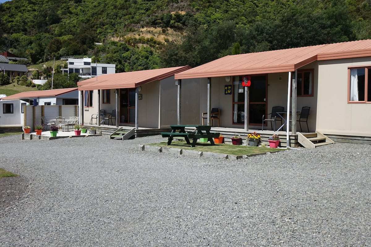 A row of single-story buildings with red roofs, outdoor seating, and a gravel ground.