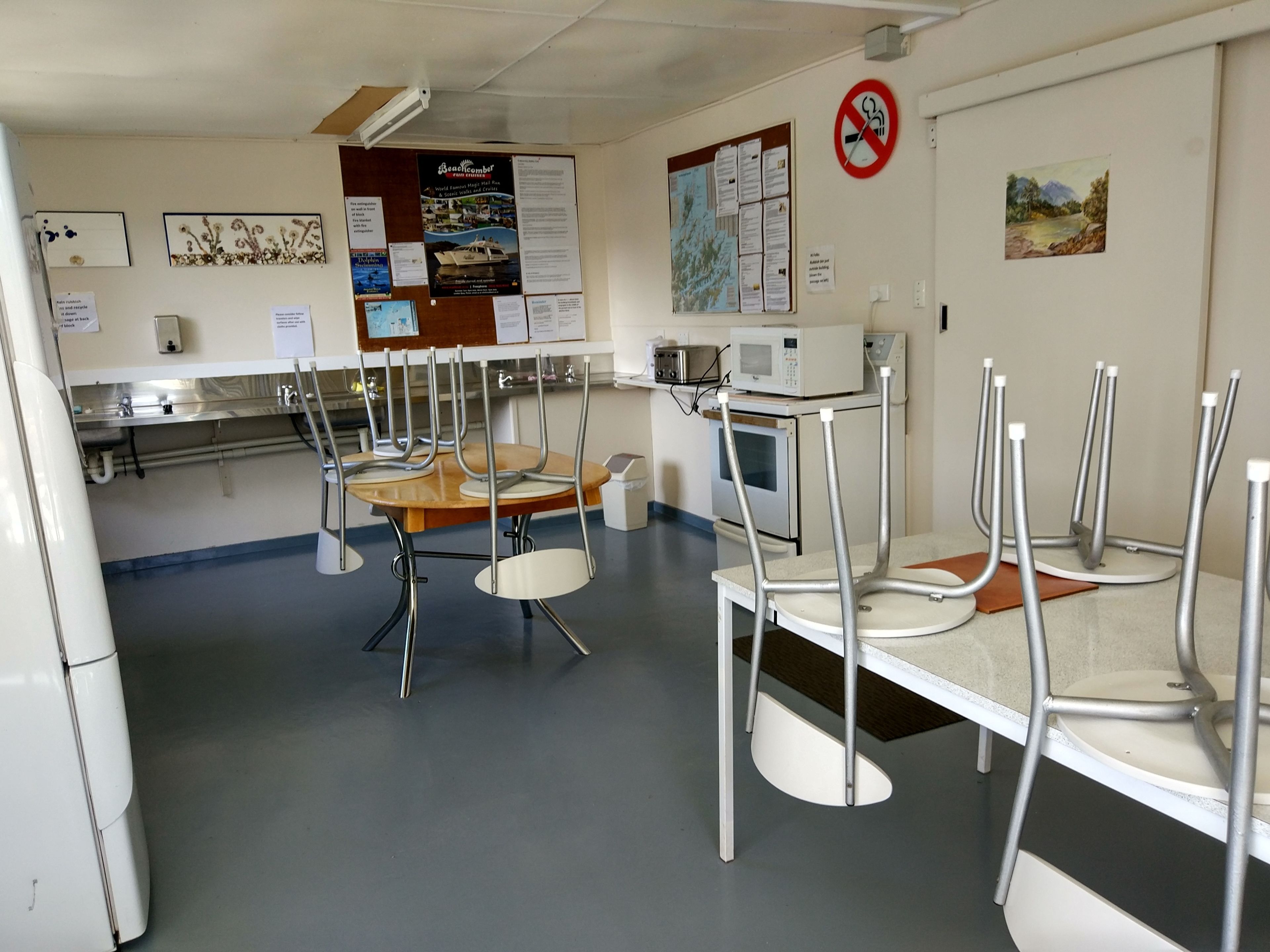 A kitchen with a dining table and chairs, a microwave, and various notices on the wall.