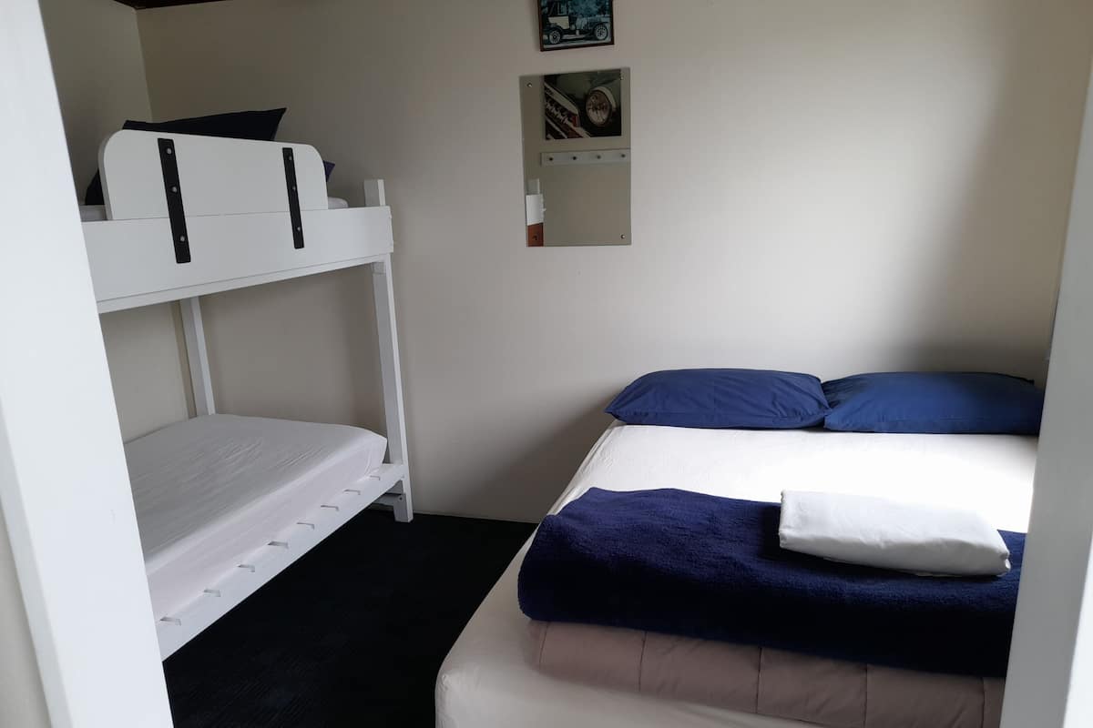 A bunk bed room with a white lower bunk and a blue upper bunk. There is a small shelf with a picture frame above the bed.