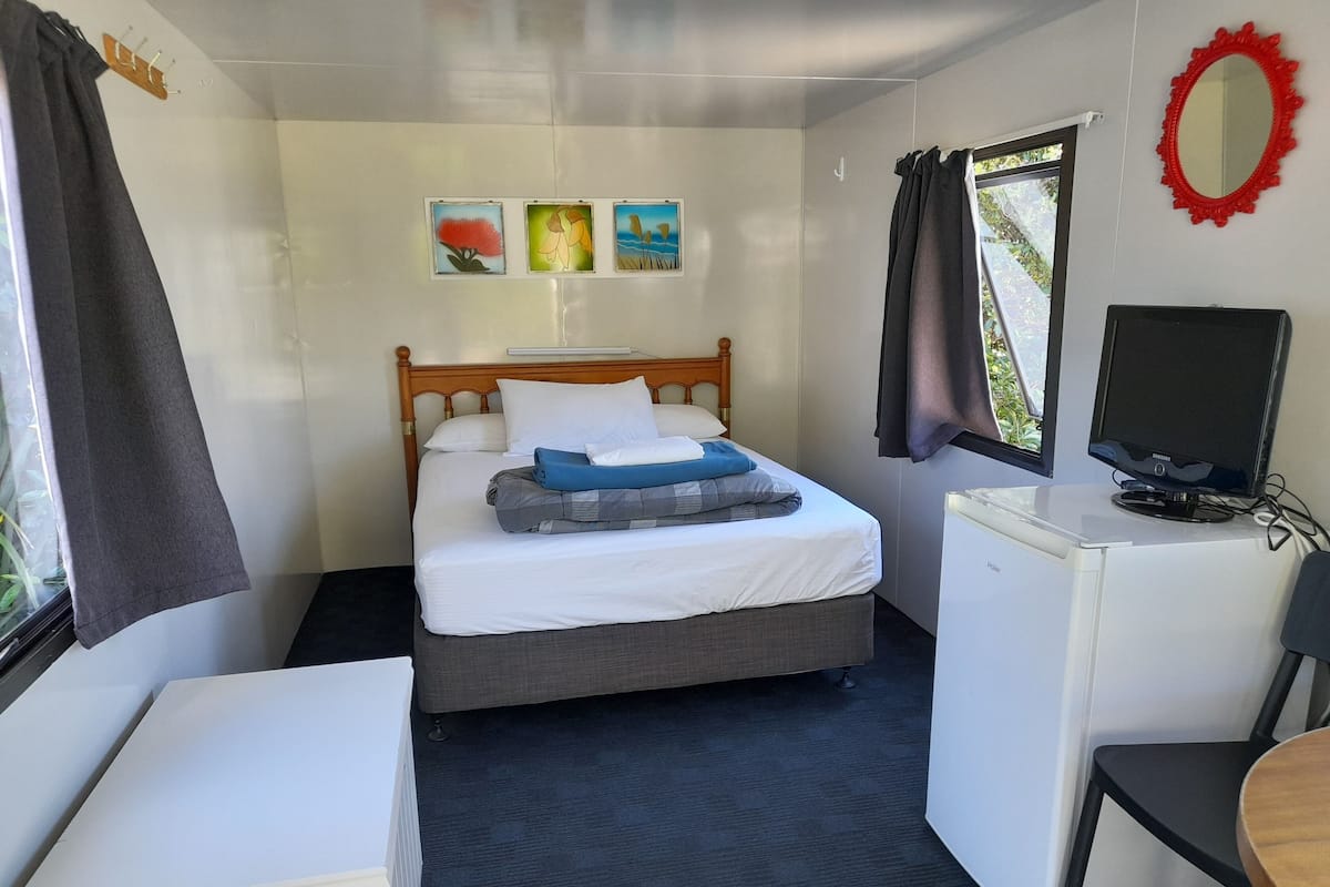 A compact room with a bed, a desk, a chair, a TV, and a window with curtains.