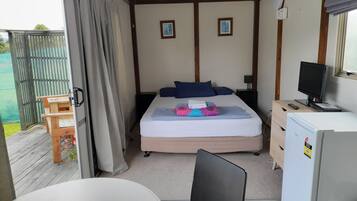 Un dormitorio con cama, escritorio, silla, televisor y refrigerador.