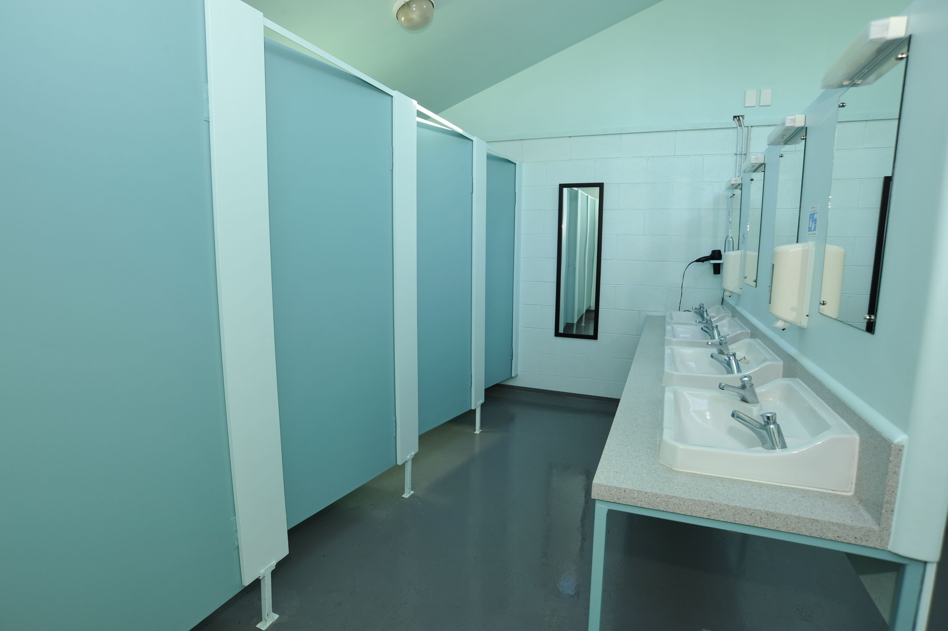 A bathroom with three sinks, a mirror, and a door leading to a changing room.