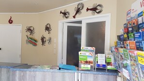 Zona de recepción con mostrador que exhibe guías de viaje, una puerta y adornos en la pared, incluyendo figuras de cangrejo y un letrero de bienvenida.