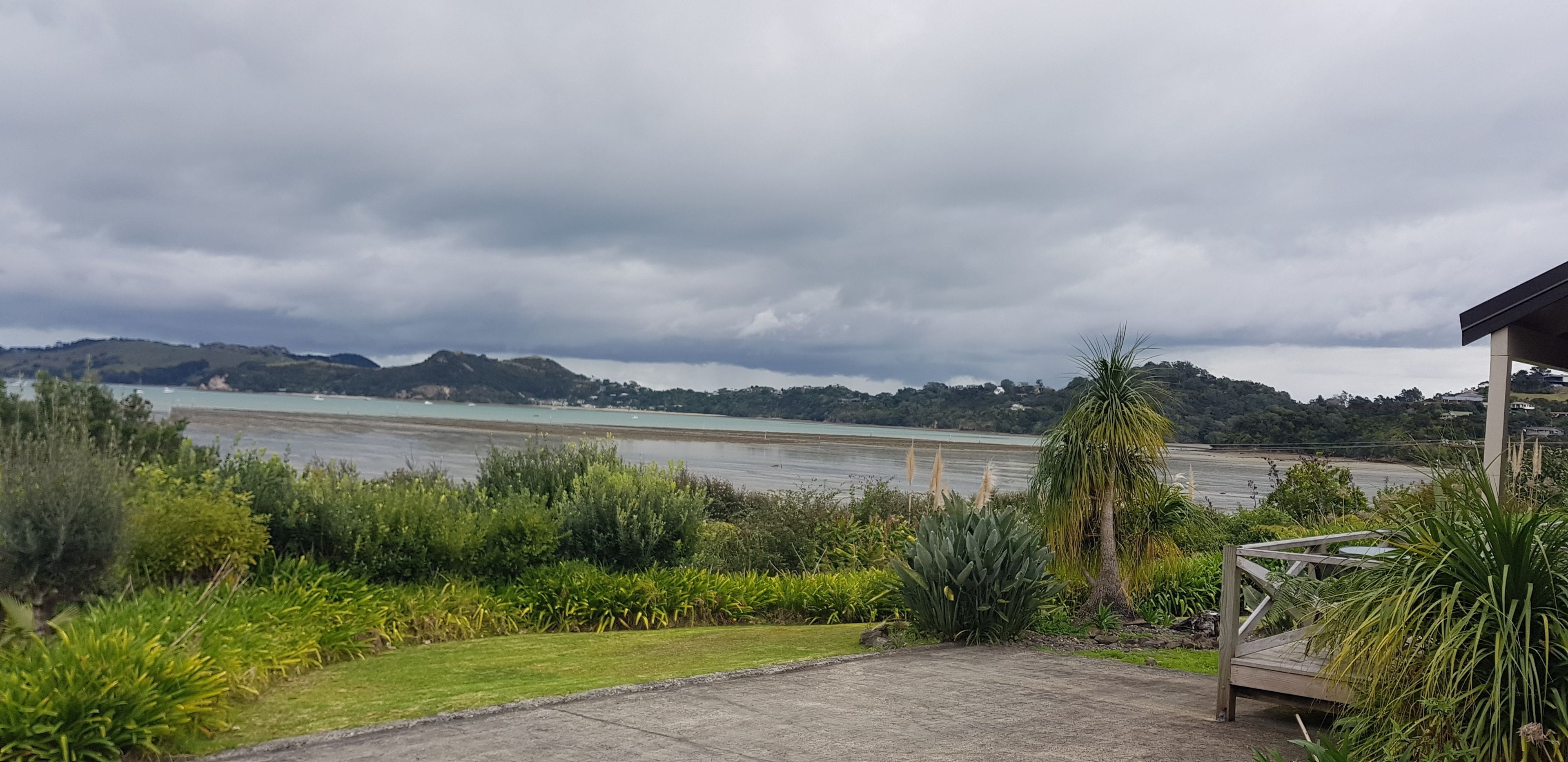A coastal view with a grassy area, a wooden deck, and a body of water under a cloudy sky.