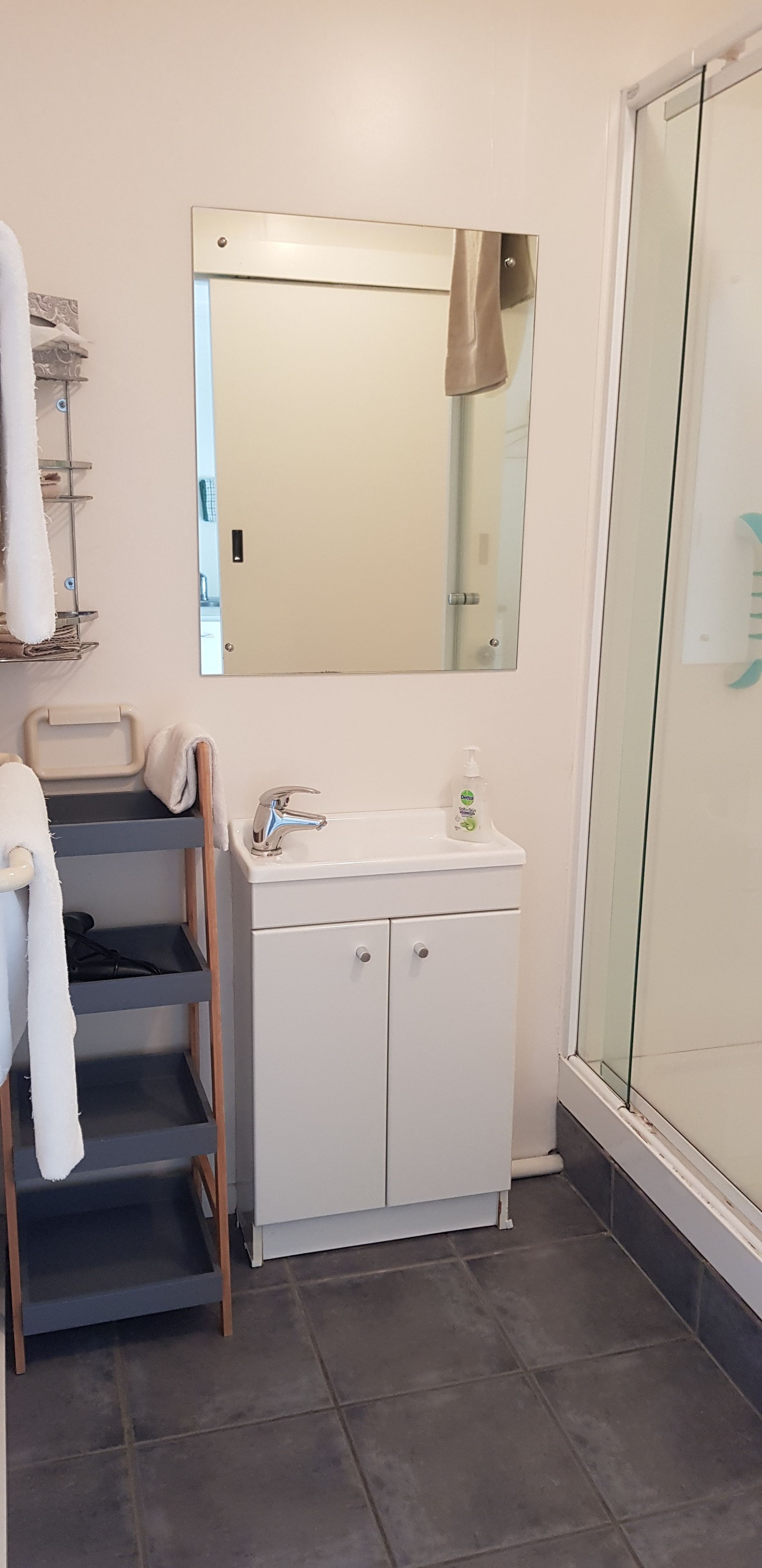 A bathroom with a white vanity, a mirror, a towel rack, and a shower area.