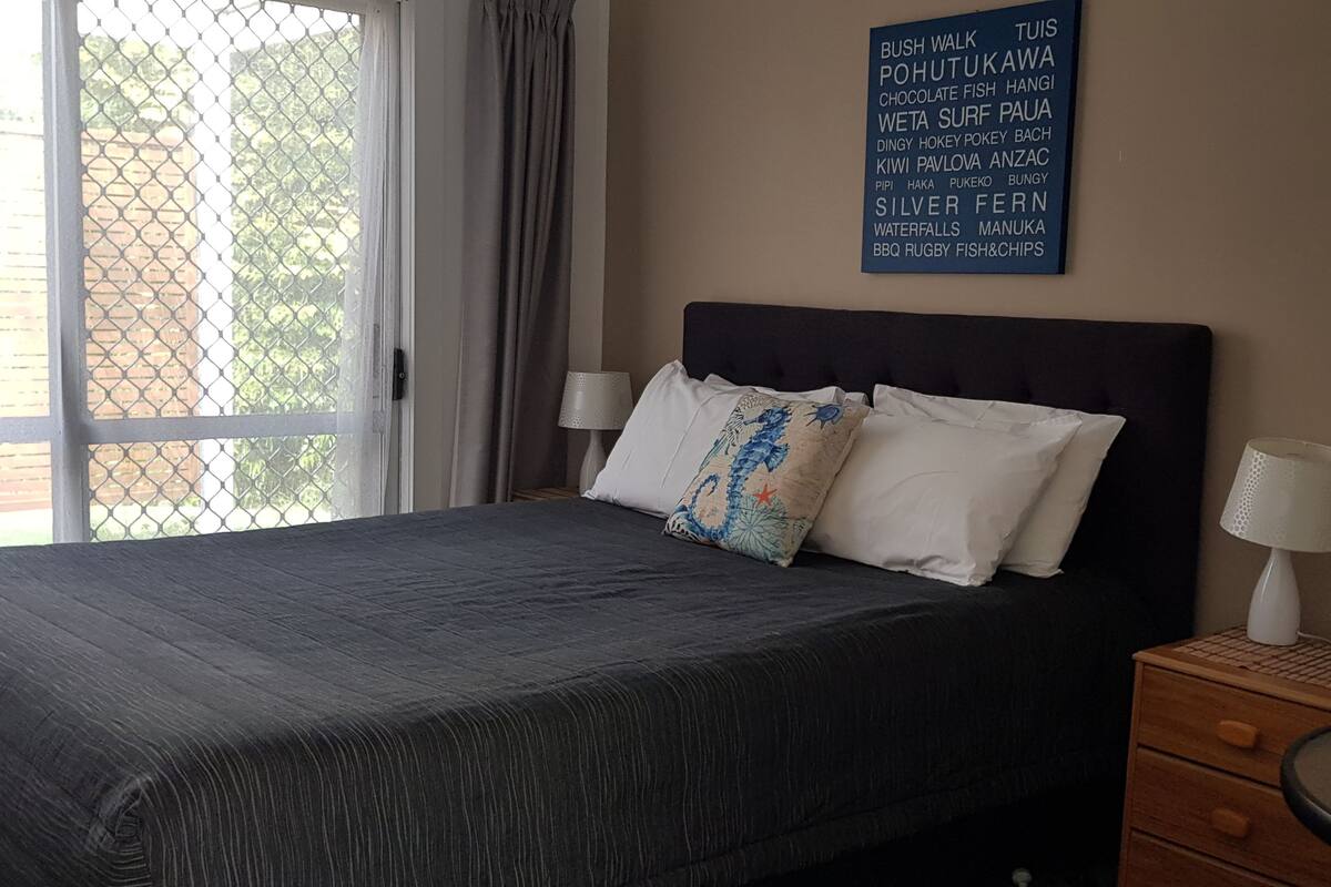Un lit bien fait, recouvert d’une couverture sombre, avec deux oreillers et un panneau fixé au mur indiquant différentes activités.