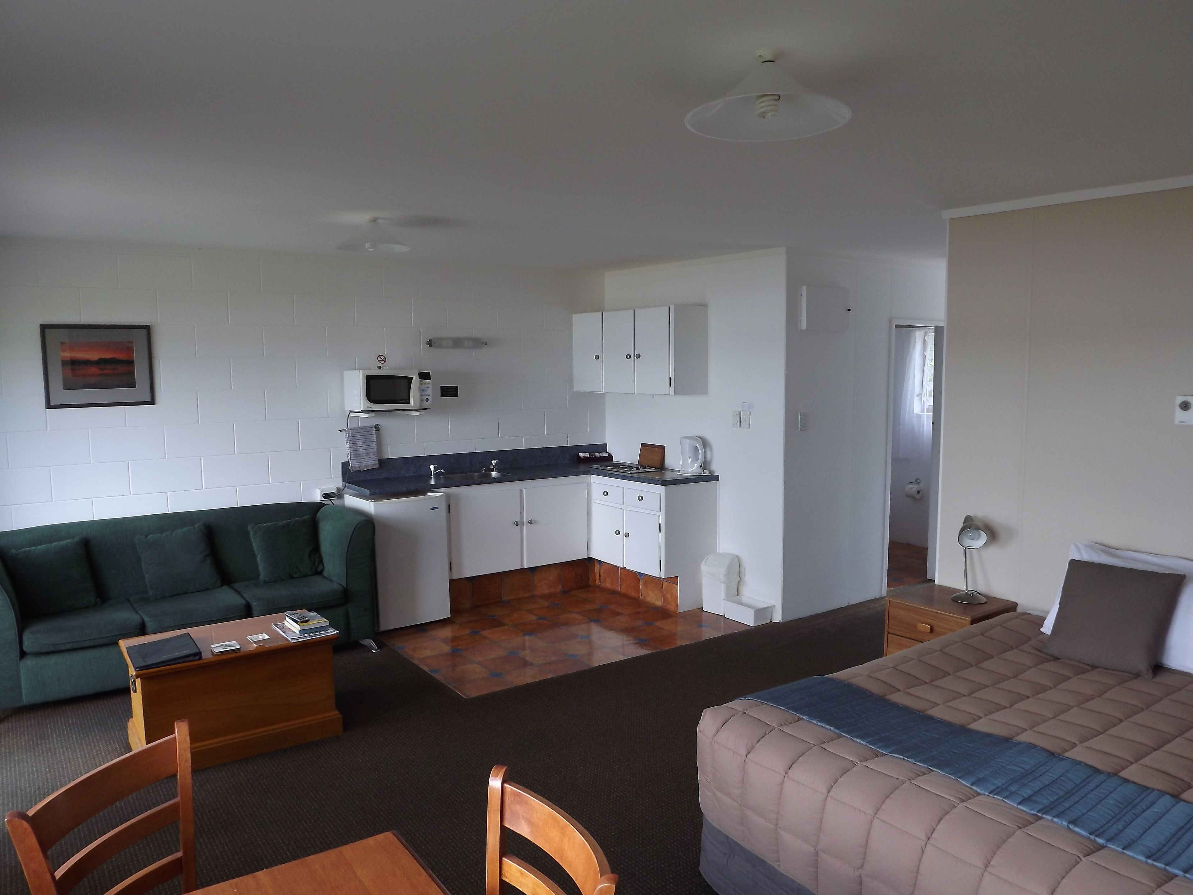 Een compacte kamer met een kitchenette, een groene bank, een bed en een houten tafel.
