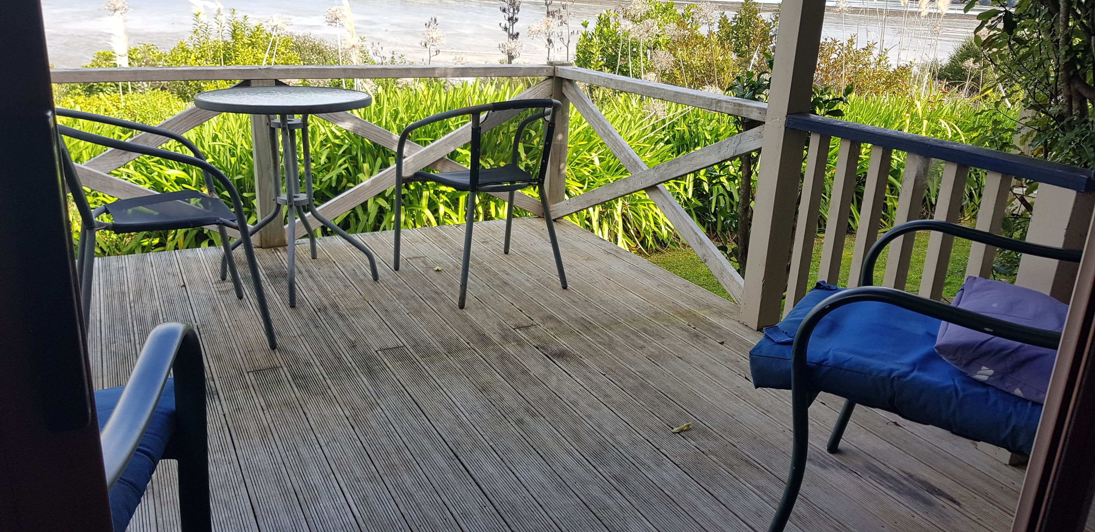 A wooden deck with metal chairs and a small table, overlooking a garden with tall plants.