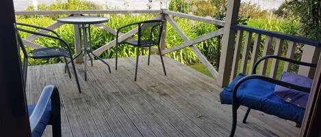 A wooden deck with metal chairs and a small table, overlooking a garden with tall plants.