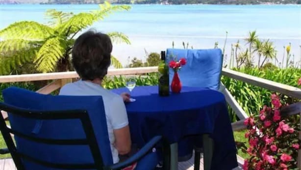 Una persona sentada a una mesa con vistas al mar y colinas al fondo.