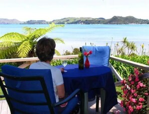 A person seated at a table with a view of the sea and hills in the background.