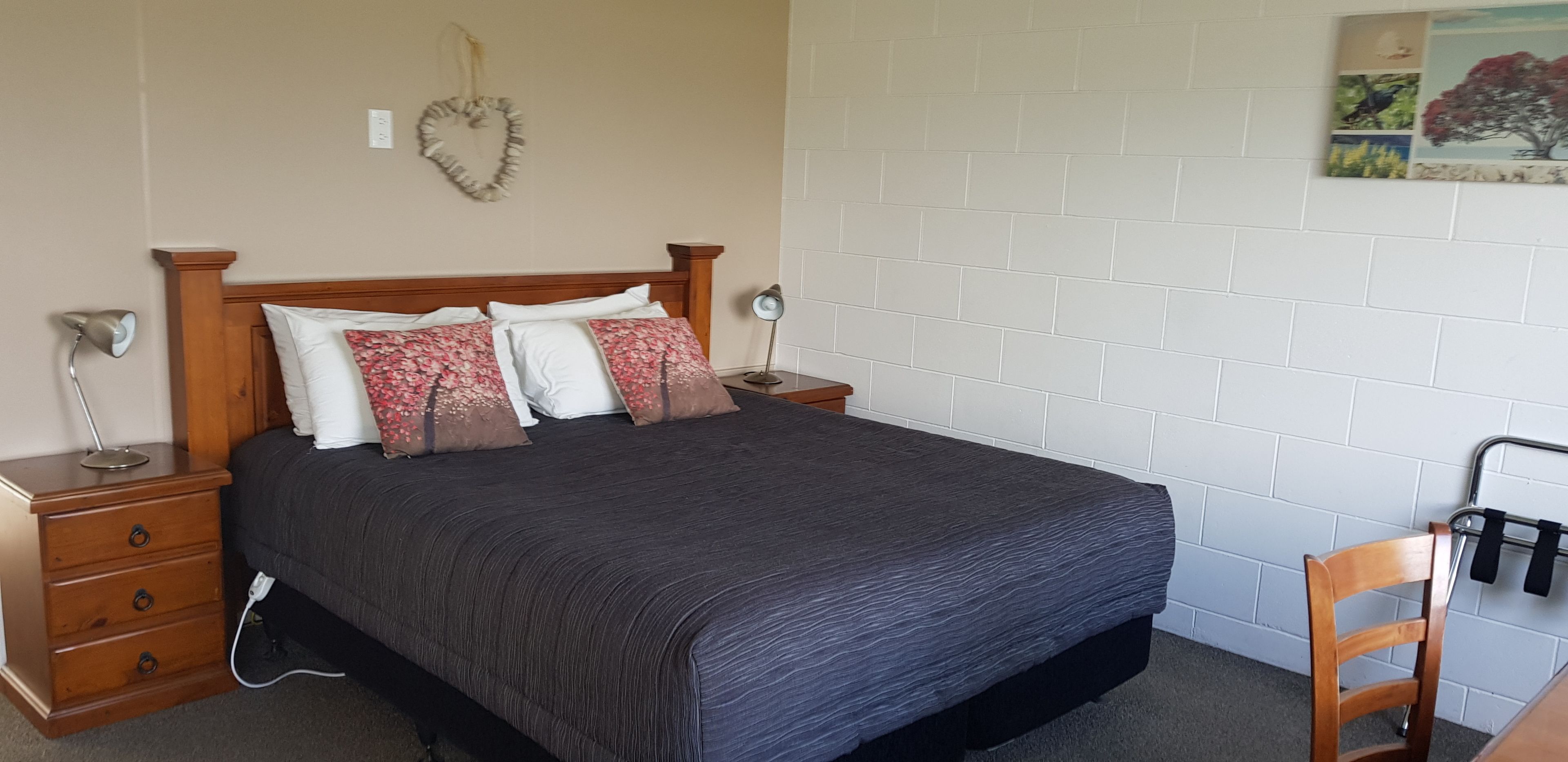 A bedroom with a large bed, two bedside tables, a chair, and a wall-mounted rack.