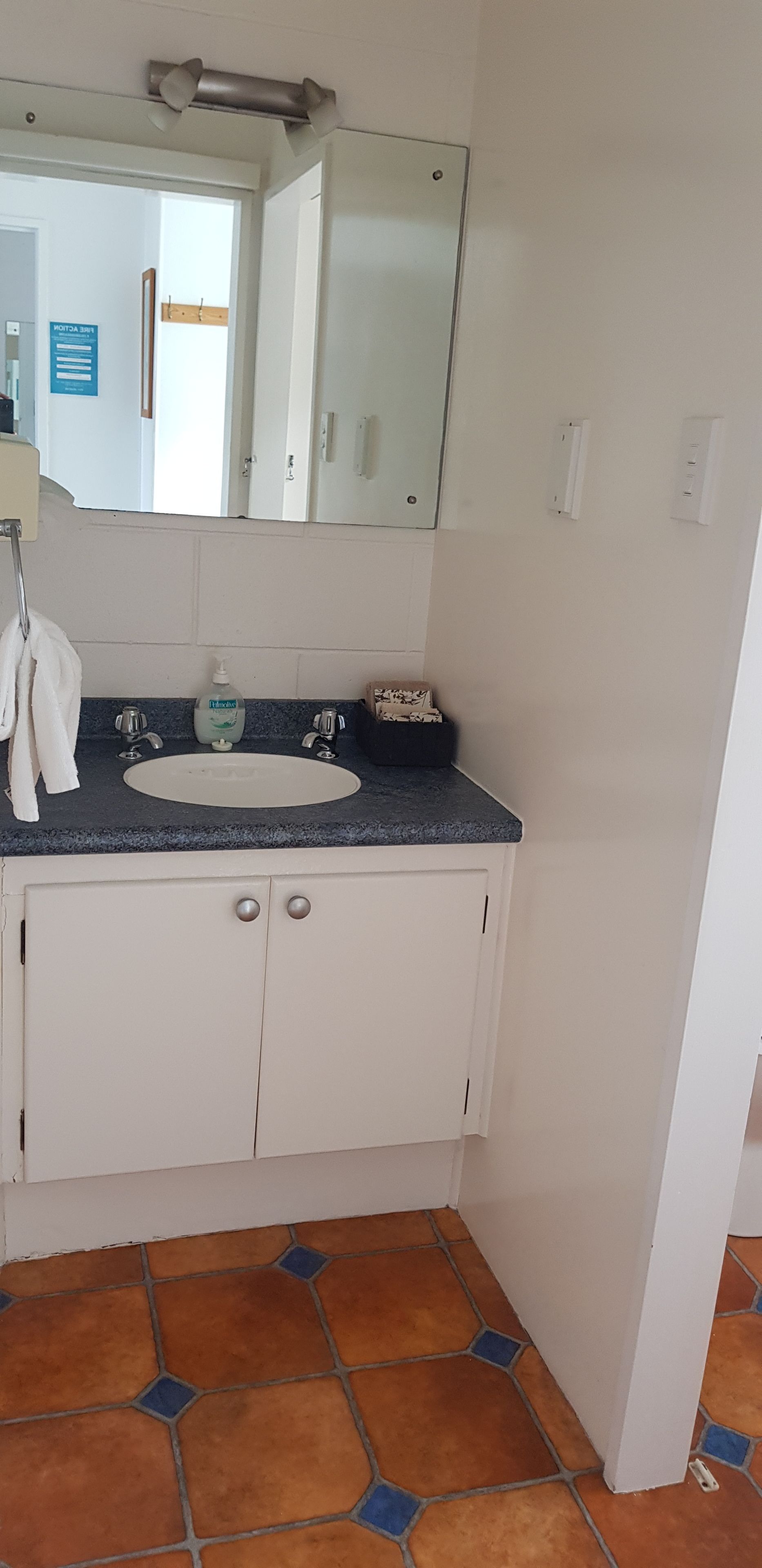 A bathroom with a white sink, two faucets, a mirror, and a towel hanging on a rack.