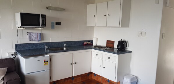 A compact kitchen with white cabinets, a built-in microwave, a sink, and a coffee maker.