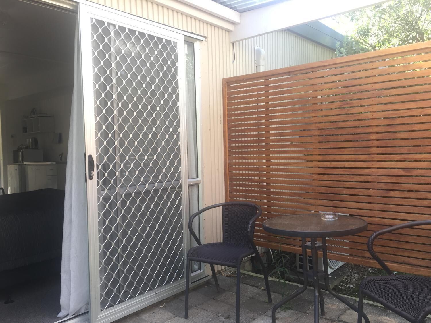 Un patio con puerta corredera de vidrio, cerca de madera y una mesa redonda con dos sillas.