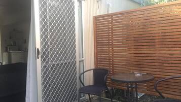 Un patio con puerta corredera de vidrio, cerca de madera y una mesa redonda con dos sillas.