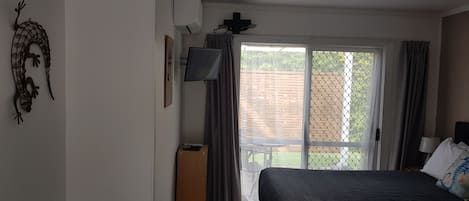 Une chambre à coucher avec un lit, une télévision, une fenêtre avec des rideaux et une vue sur l’extérieur.
