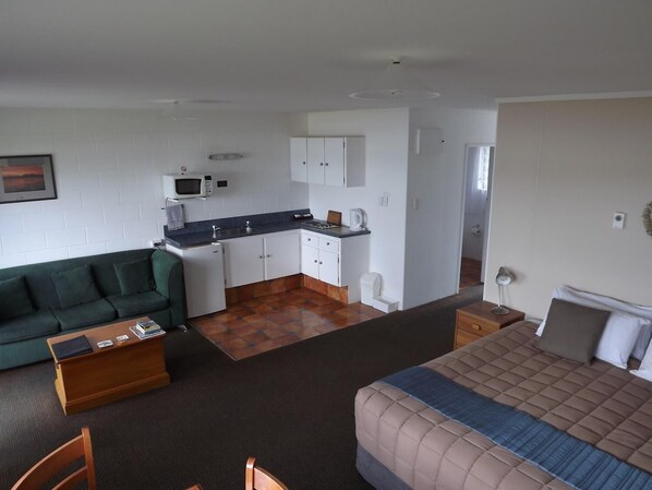 A compact room with a kitchenette, a green sofa, a bed, and a small wooden table. - Harbour View Motel Coromandel (Coromandel)
