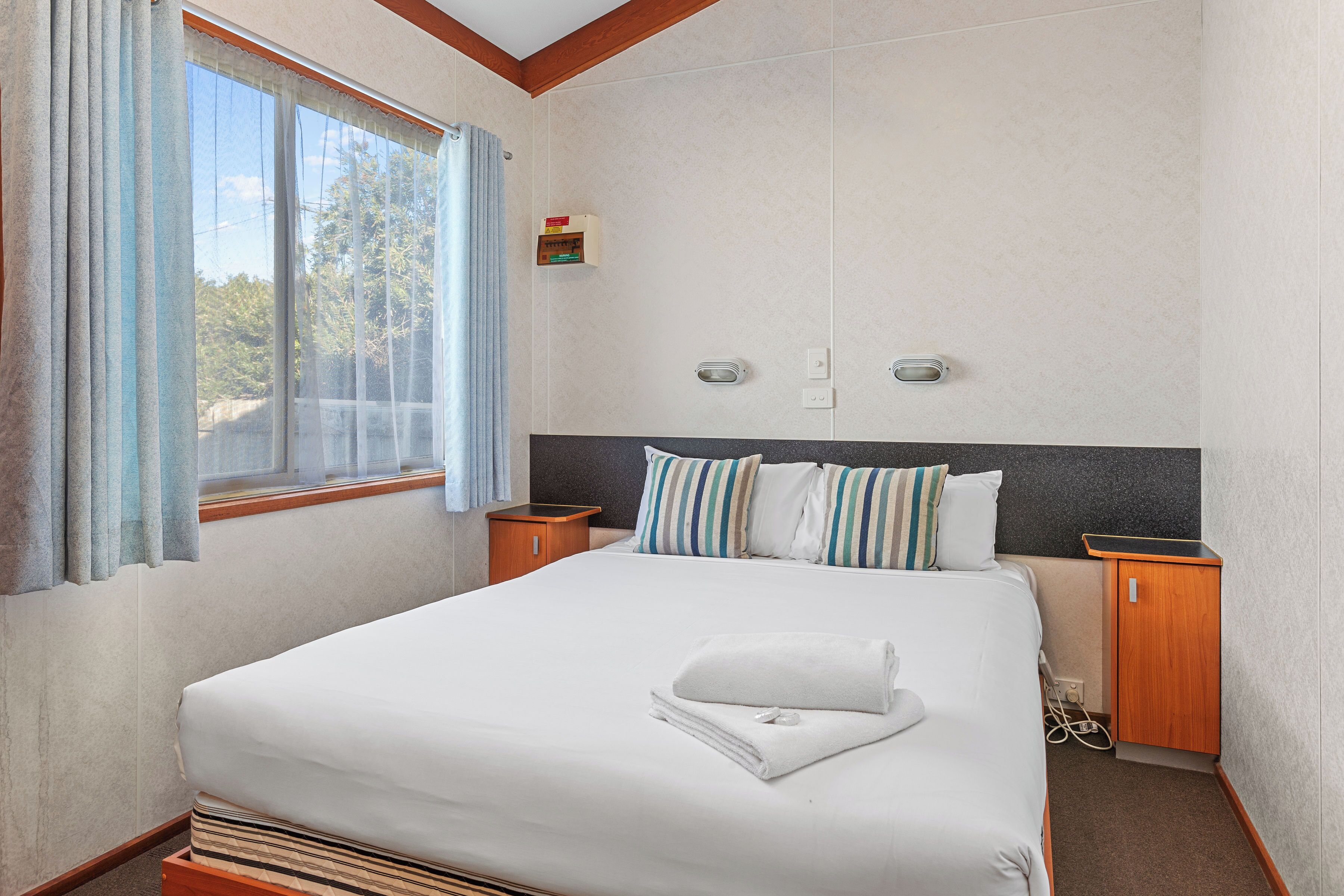 Una habitación de hotel con una cama grande, una ventana con cortinas, una mesita de noche y un armario pequeño.
