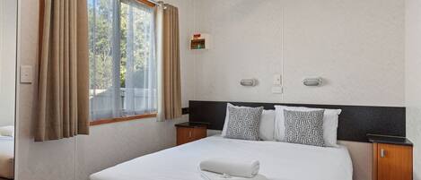 Una habitación de hotel con una cama grande, una mesita de noche, cortinas en una ventana y una lámpara de pared.