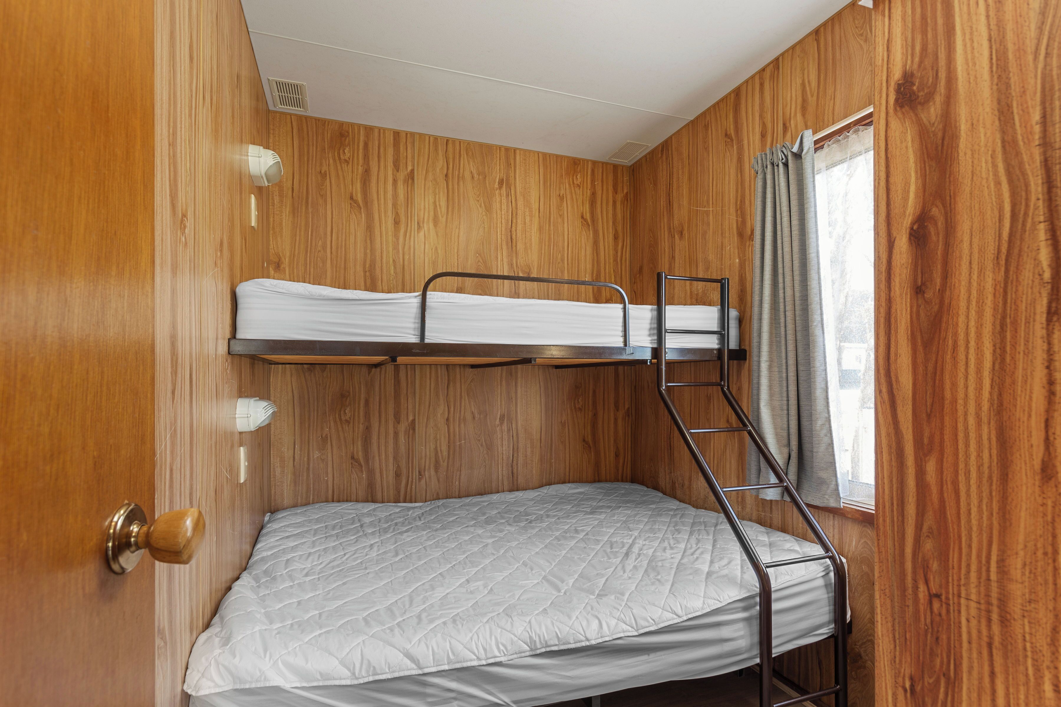 Une chambre avec un lit superposé, des murs en bois, une fenêtre avec des rideaux et une porte dotée d’une poignée.