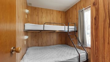 Une chambre avec un lit superposé, des murs en bois, une fenêtre avec des rideaux et une porte dotée d’une poignée.