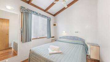 A bedroom with a bed, a nightstand, a ceiling fan, and a window with curtains.