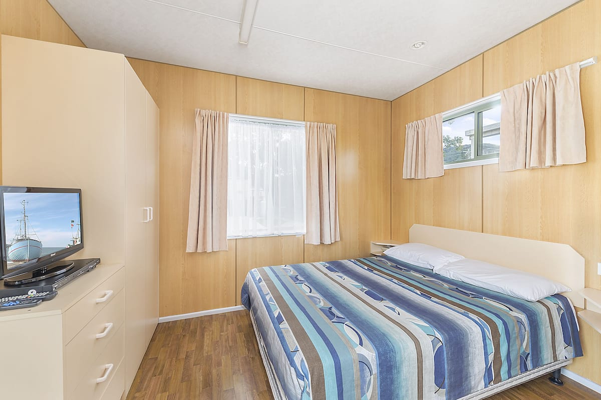 A bedroom with a bed, curtains, a television, and a window.