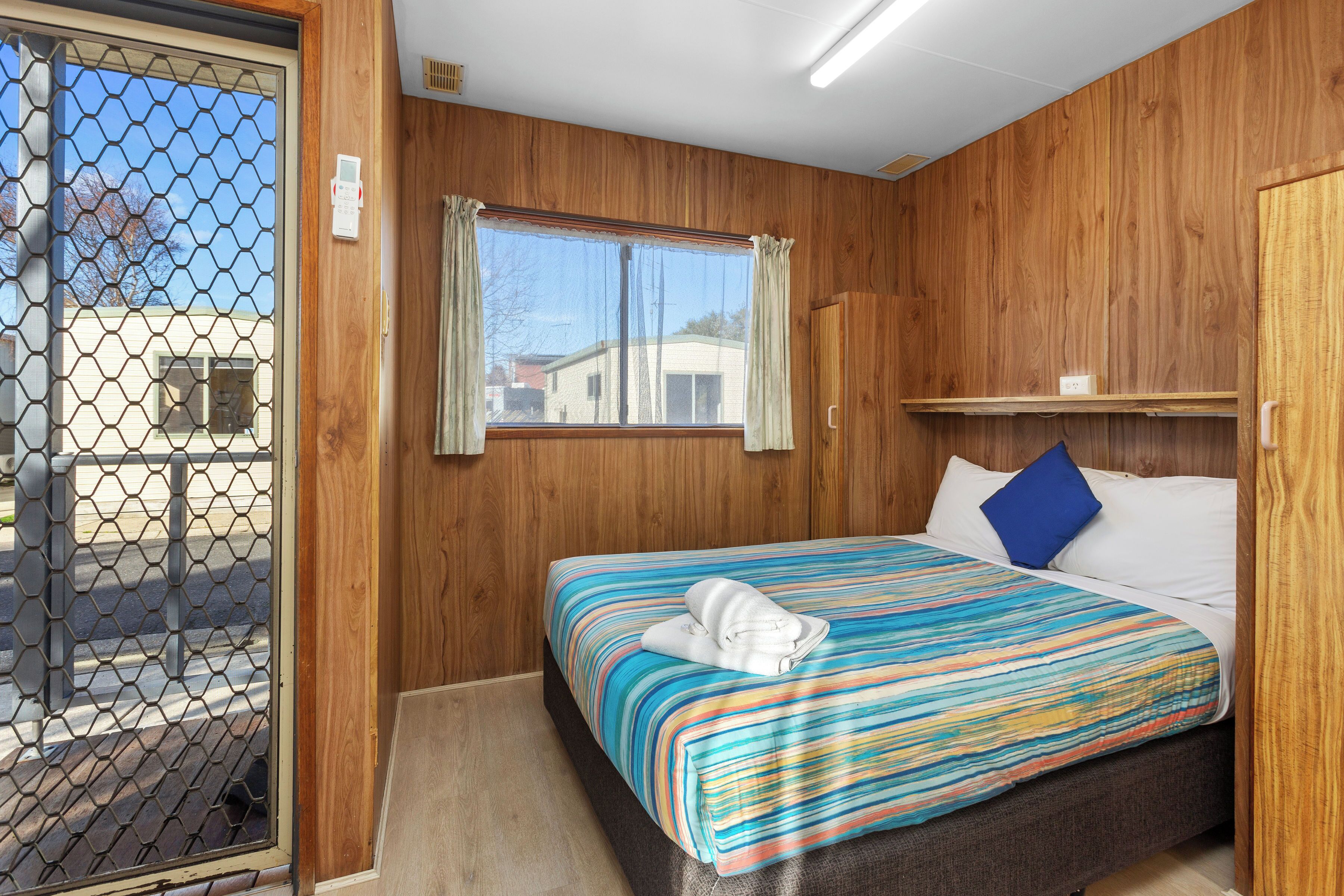 A single bed with a striped bedspread, a window with curtains, and a wooden wall.