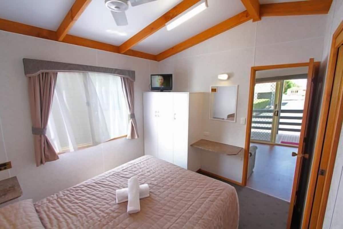 A bedroom with a bed, a wardrobe, a mirror, and a window with curtains.