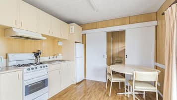 A compact kitchen with a stove, oven, and refrigerator. There is a dining table with chairs and a sliding door closet.