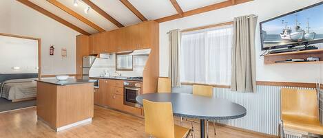 A modern kitchen with wooden cabinets, a dining area with a round table and yellow chairs, and a large window with curtains.