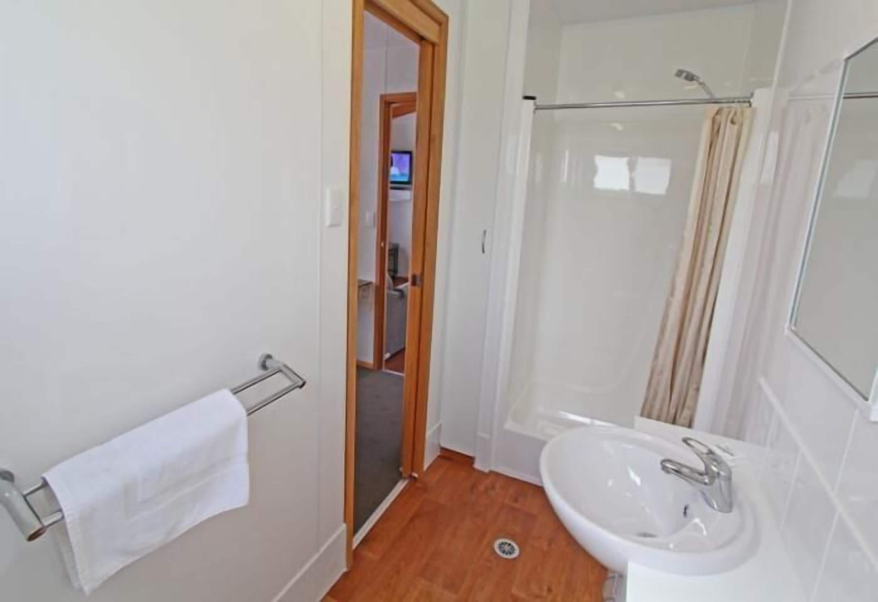 A bathroom with a glass shower enclosure, a white sink, and a towel rack.