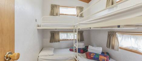 A bunk bed room with wooden beams, white walls, and curtains on windows.