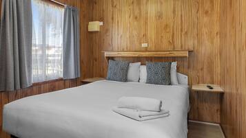 Ein Hotelzimmer mit einer holzverkleideten Wand, einem Bett mit weißer Bettwäsche, grauen Vorhängen und einem Nachttisch mit einer Lampe.