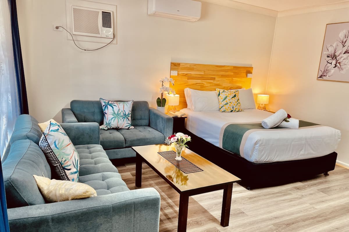 A hotel room with a sofa, a bed, a bedside table, and a lamp.