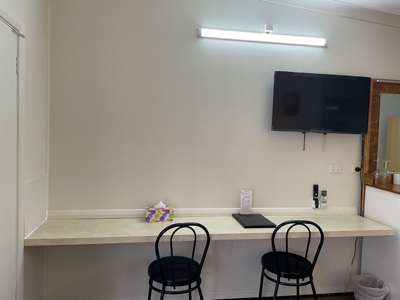 A small, private office with a desk, two chairs, a flat-screen TV, a desk lamp, a tissue box, and a small trash bin.