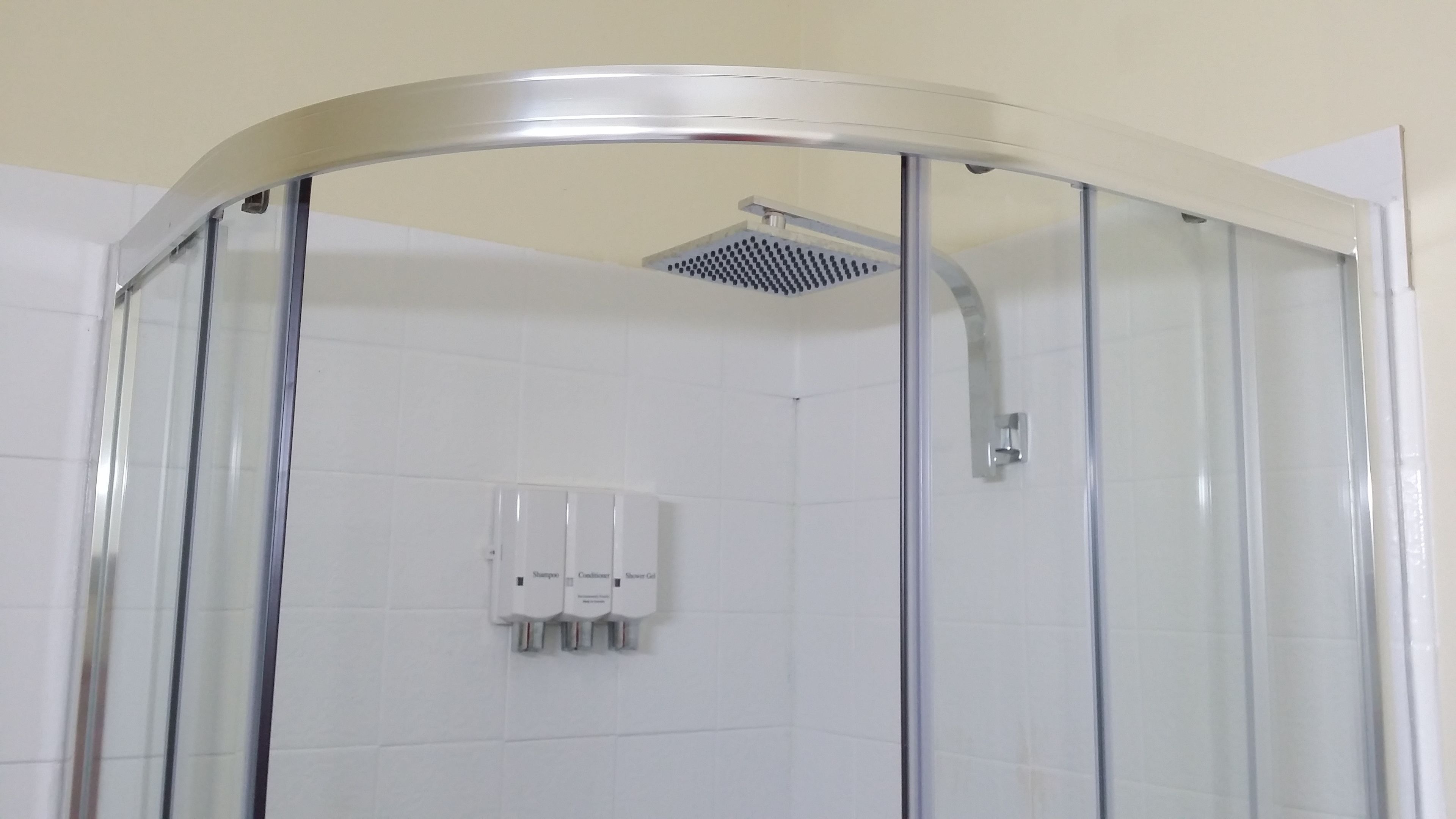 A glass-enclosed shower with a handheld showerhead and a wall-mounted soap dispenser.