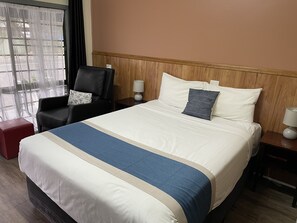 A hotel room with a large bed, a chair, a nightstand, and a window with sheer curtains. - Highway Motor Inn (Taree)