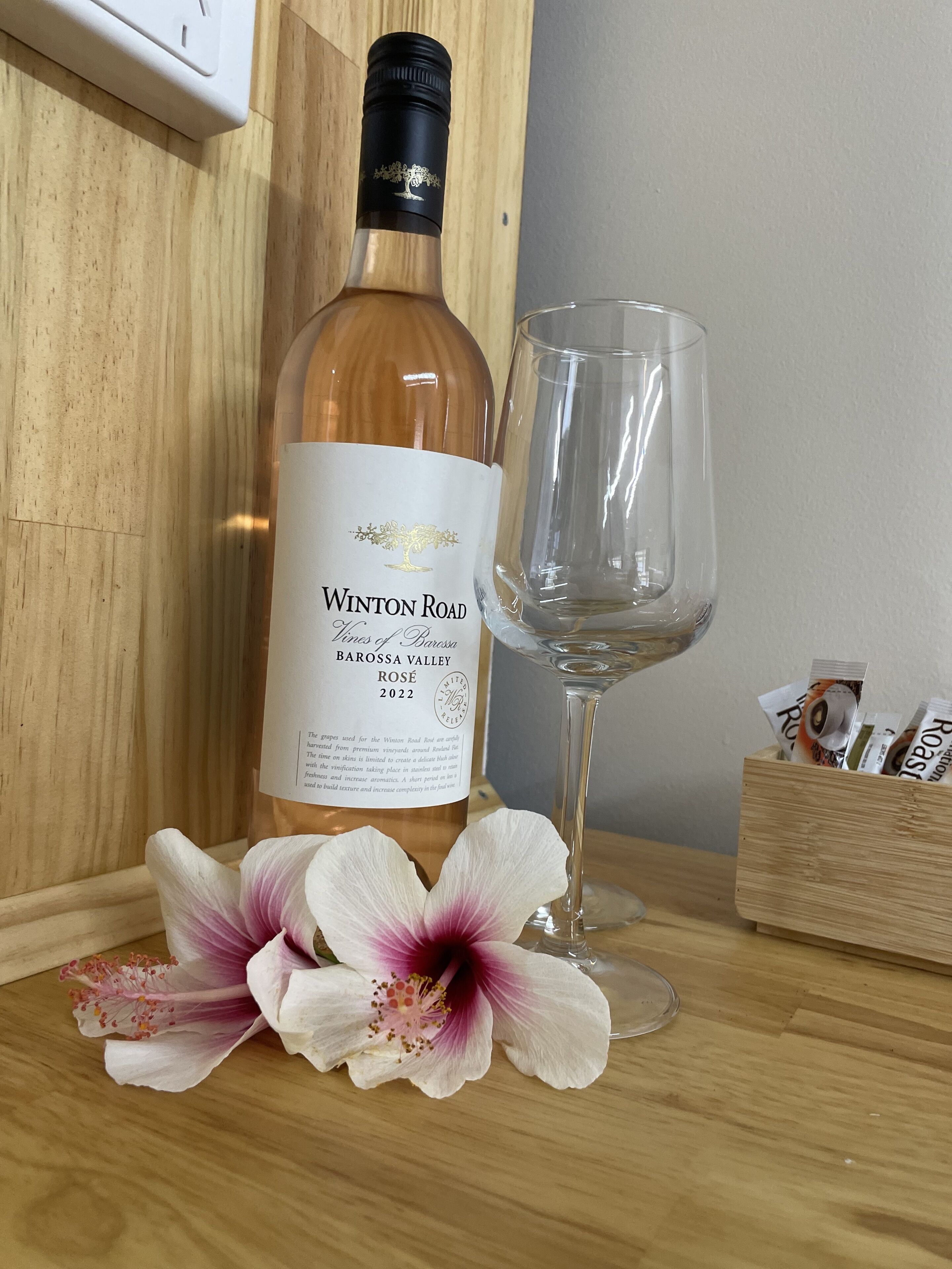 Eine Flasche Winton Road Wein, ein Glas und eine Holzkiste mit Packungen auf einer Holztischplatte.
