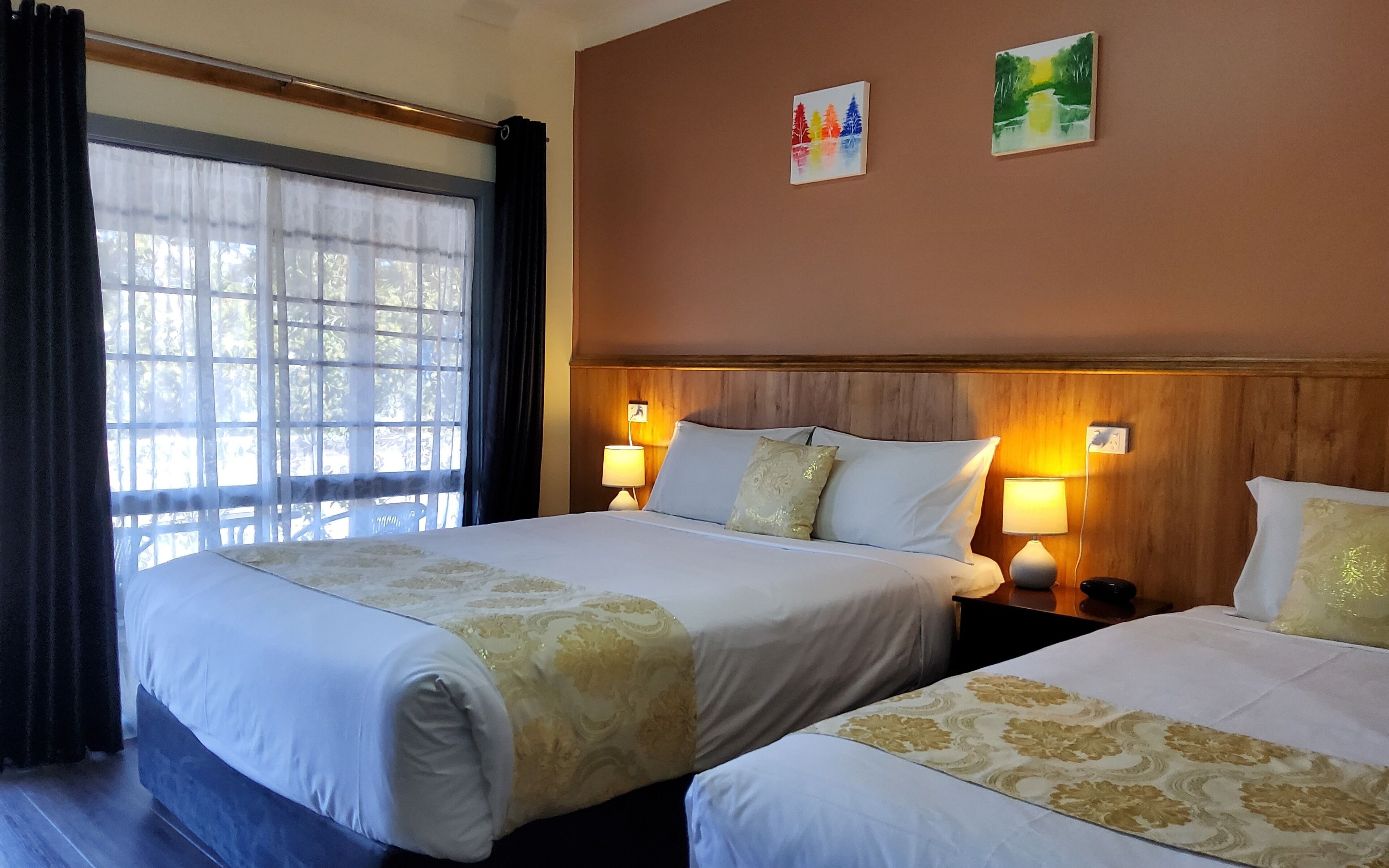 A hotel room with two beds, a wooden headboard, two bedside lamps, and a window with curtains.