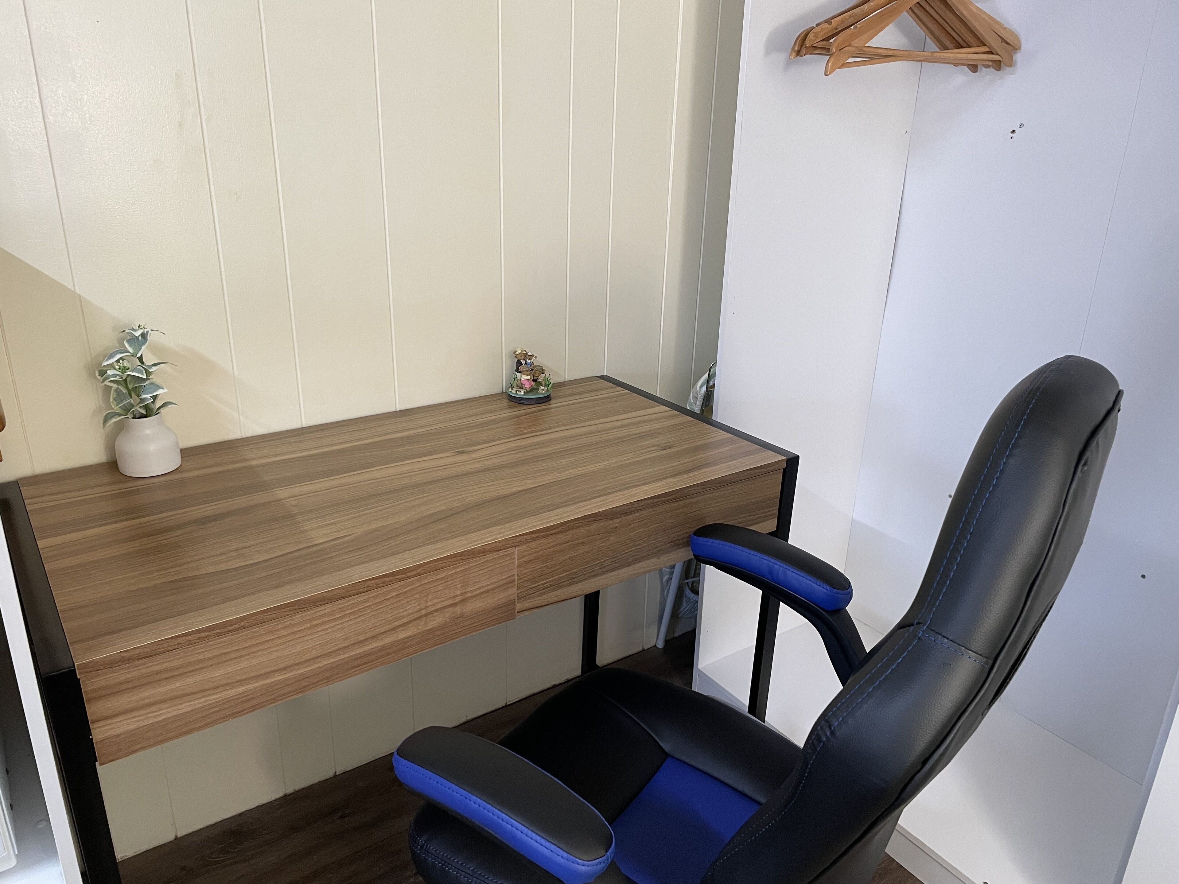Een houten bureau met een blauwe stoel, een kleine plant en een houten kapstok.