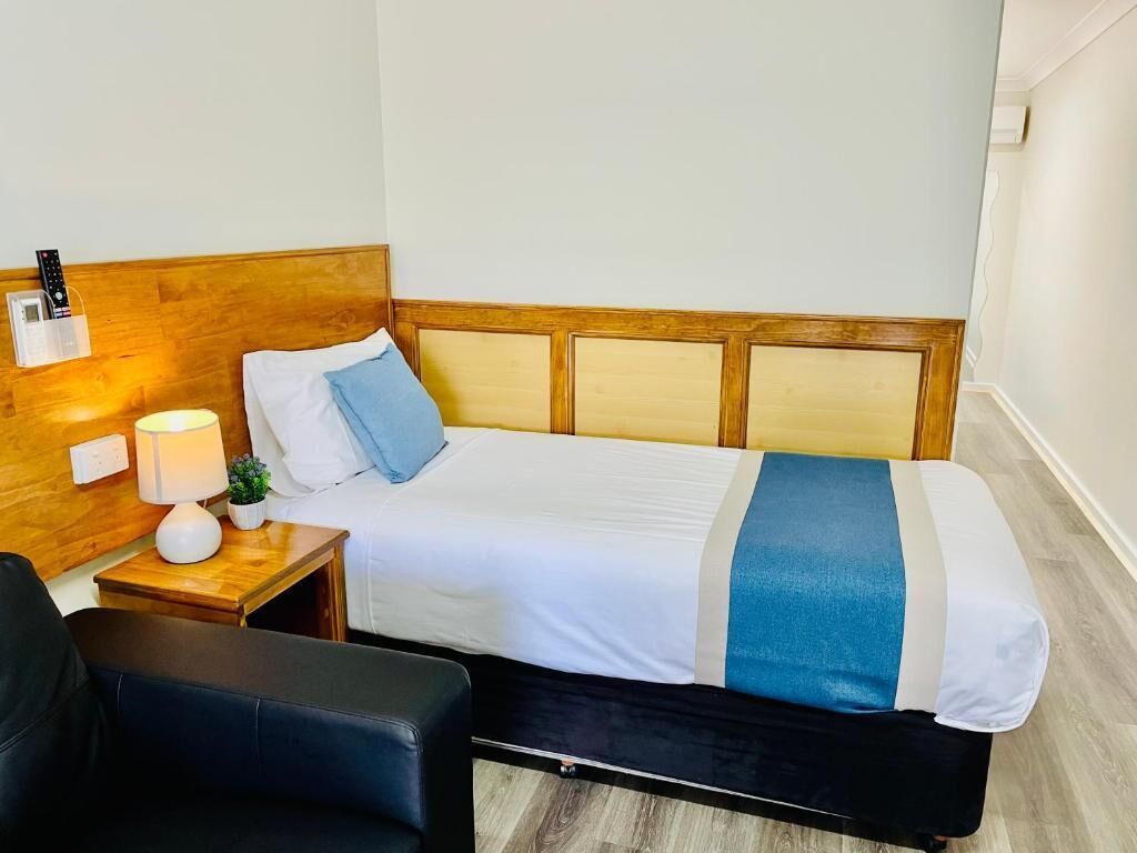 A neatly made bed with a wooden headboard, a bedside lamp, and a small plant on the nightstand.