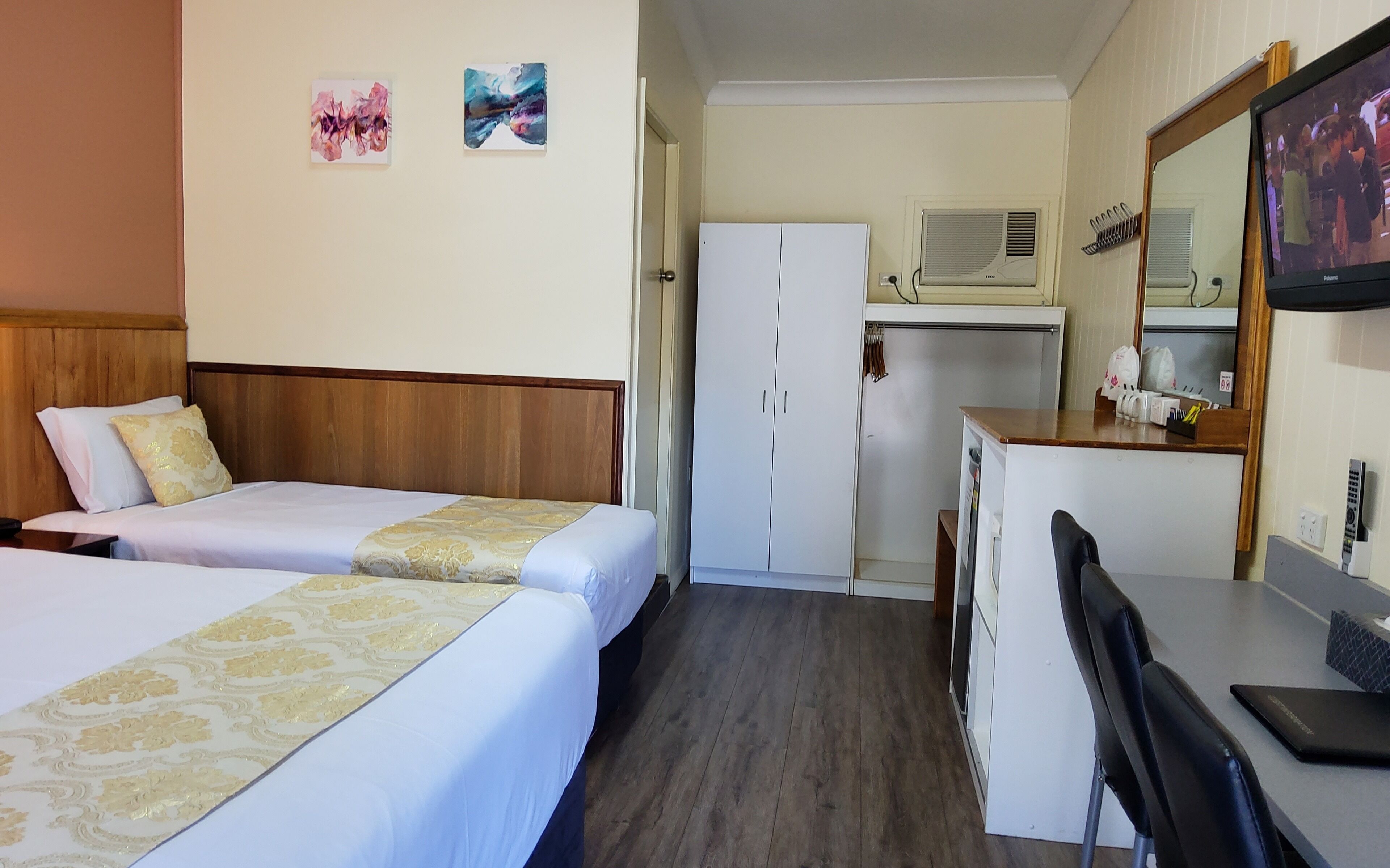 Una habitació d'hotel amb dos llits, una taula de treball, un mirall i una televisió.