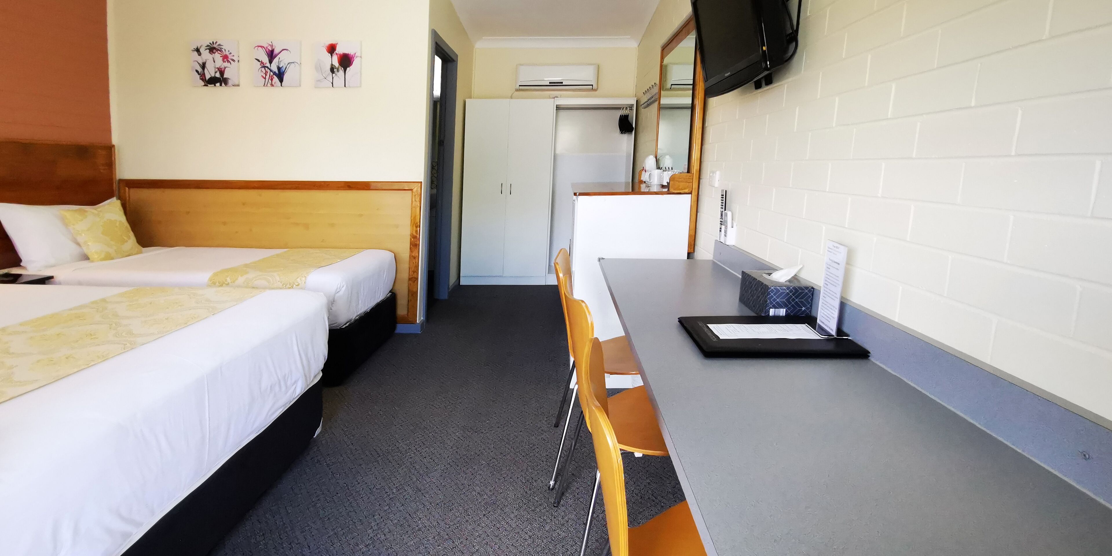 Ein Hotelzimmer mit zwei Betten, einem Schreibtisch, einem Sessel, einem Fernseher und einem Kleiderschrank.